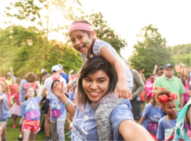 A Girls on the Run 5K participant smiles while holding a smaller child on her shoulders